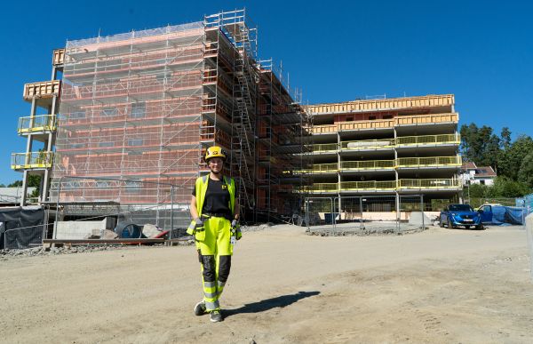 Energiingeniør Ragna Gjerstad iført synlighetsklær og verneutstyr står foran et boligkompleks som er under utbygging.