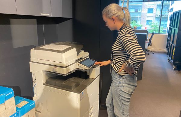 Supportkonsulent Yvonne Skaugen står ved en kopimaskin. Hun trykker på en liten skjerm. 