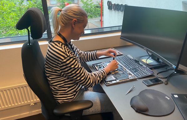 Supportkonsulent Yvonne Skaugen sitter ved en kontorpult og skrur på en harddisk. Det er en stor pc-skjerm på kontorpulten.