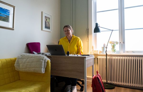 Ingebjørg sitte bak skrivebordet sitt og arbeider på en datamaskin. Hun har gul genser på seg. 