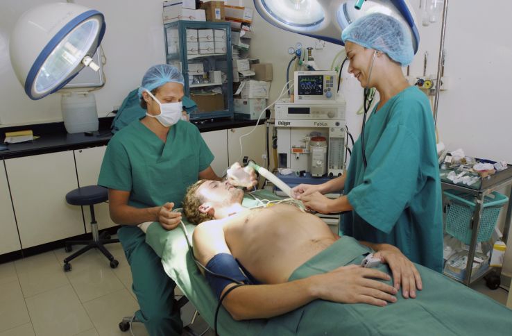Mannlig pasient på sykeseng blir behandlet av anestesilege og operasjonssykepleier før operasjon.