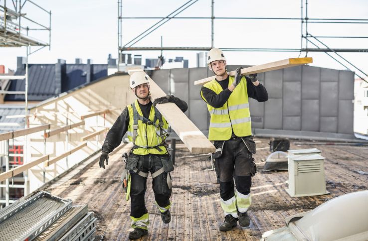 To arbeidere på byggeplass bærer materialer.