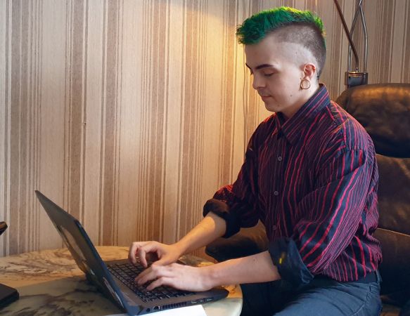 Mann med grønn hanekam sitter foran laptop og skriver.