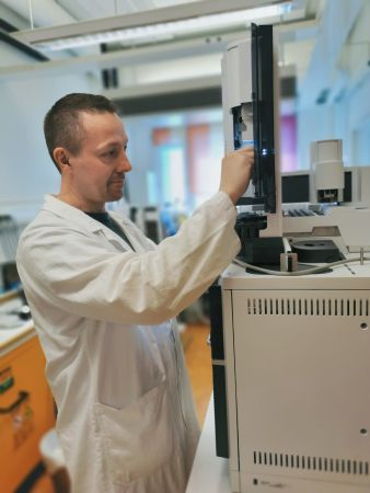 Mann i hvit frakk står foran en maskin i laboratoriet