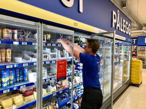 Mann i blå t-skjorte plasserer varer i hylla i kjøleskap.