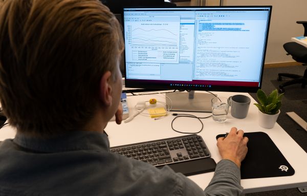 Ung mann sitter ved skrivebord og viser et statistikkprogram på dataskjermen.
