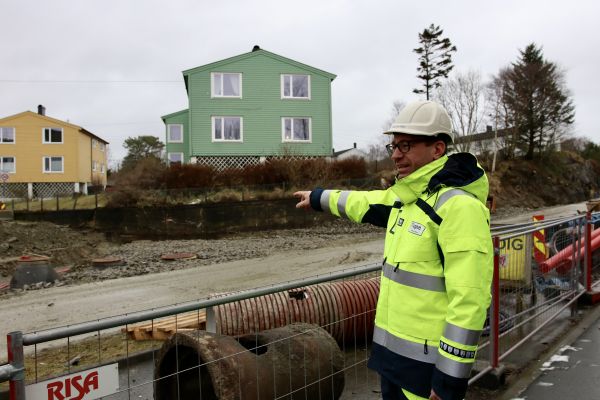 Elektroingeniør Johannes Olsen er avbildet foran et område der det graves. Han er iført hvit hjelm og gul arbeidsjakke, og peker inn mot anleggsområdet. 