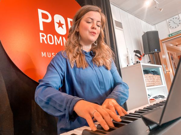 Kvinne med blå skjorte sitter ved et piano og spiller