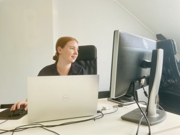 Spilldesigner Maria Engell sitter ved et arbeidsbord og ser på to dataskjermer