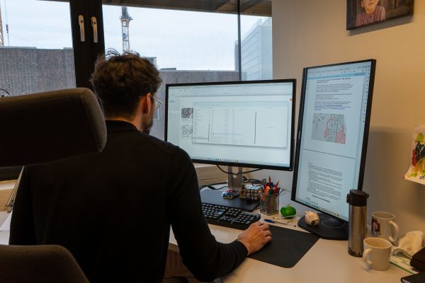 Mann sitetr ved skrivebord og ser på en datamaskin.