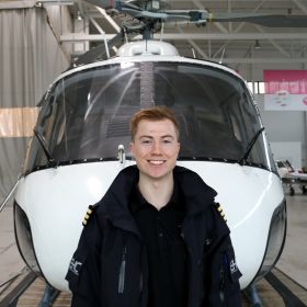 Oskar Emil Olafsen poserer foran et helikopter. 