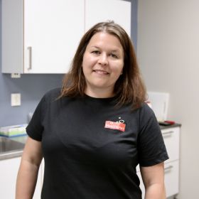 Matteknolog Kari Haugstad er avbildet inne på et av laboratoriene der hun jobber. Hun er iført svart T-skjorte med logo fra Mattilsynet, og er avbildet fra livet og opp. Hun smiler og har mørk, langt hår. 