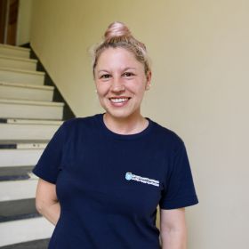 Renholdsoperatør Maricela Naprica er avbildet på Haugesund rådhus, som er et av byggene hun rengjør. Hun har langt, lyst hår satt opp i en knute, og er iført en mørkeblå T-skjorte med Haugesund kommune-logo. 