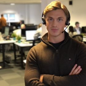 Telefonselger Kristoffer Bjørkamo står i lokalet han jobber med headsetet han bruker når han ringer på.