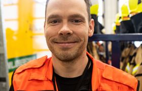 Portrettfoto av Lufthavnbetjent Glenn Olsen med orange arbeidsvest på
