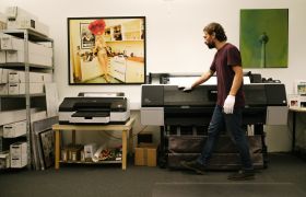 En grafisk produksjonstekniner står ved en stor printer 