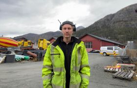 Portrettbilde av vei- og anleggsarbeider Tobias Vilhelmsen med hørselsvern, svart genser og gul arbeidsjakke. 
