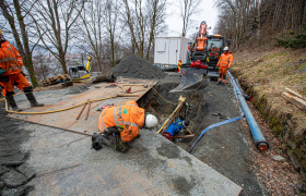 Anleggsrørleggere graver ned et stort rør i en vei.