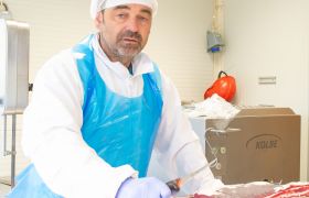 Kjøttskjærer Jan Morten i arbeidsklær holder på et stykke med ribbein