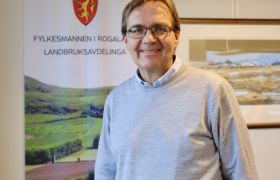 Landbruksdirektør Geir Skadberg er avbildet på kontoret sitt. Han er iført grå genser, har mellomblondt hår og briller. Han ser i kamera og smiler. 