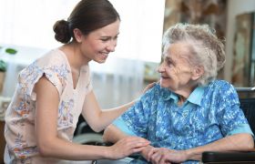Kvinnelig hjemmehjelper snakker og smiler til eldre kvinne.