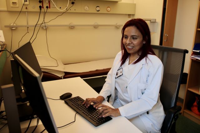 Onkolog Esperanza Sanchez er avbildet inne på kontoret sitt. Hun er iført hvite legeklær, og sitter og skriver på en pc. 