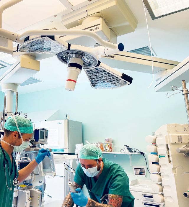 Anestesisykepleier Petter Støvind står sammen med en kollega over operasjonsbordet med et instrument i hånden.