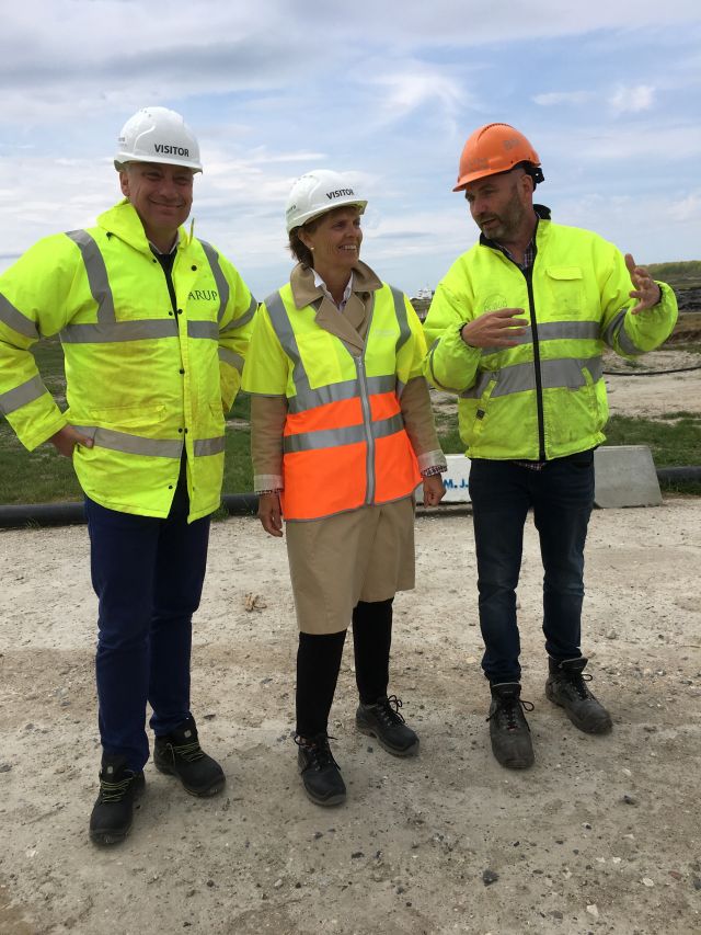 Ambassadør Aud Kolberg mellom to menn på besøk på en byggeplass iført hjelm og refleksvest