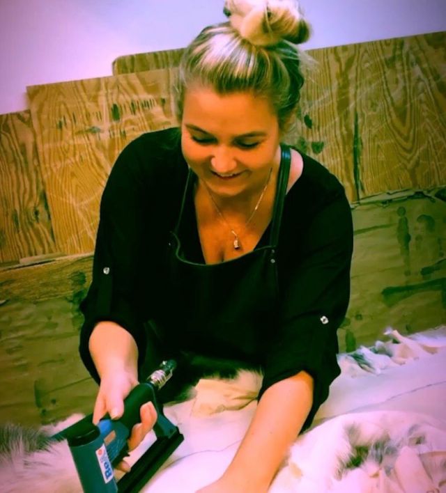 Buntmaker Jannicke Romøren Eriksen smiler mens hun ser ned på en pelsbit hun jobber med. I hendene har hun en stiftemaskin.