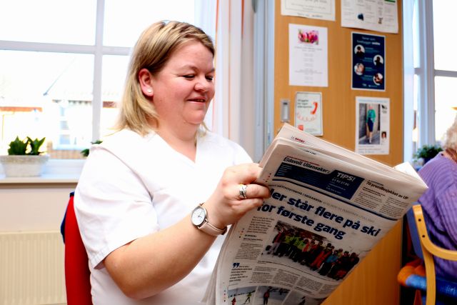 Dame i hvit sykepleieruniform holder en avis foran seg