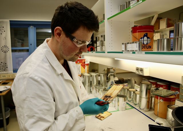Kjemiingeniør Anders Solli på lab, undersøker ei stålplate med rust, Iført kvit laboratoriefrakk og vernebrillar. 