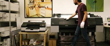 En grafisk produksjonstekniner står ved en stor printer 