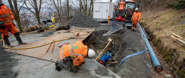 Anleggsrørleggere graver ned et stort rør i en vei.