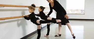 Ballettinstruktør hjelper to jenter med å utføre en arabesque.