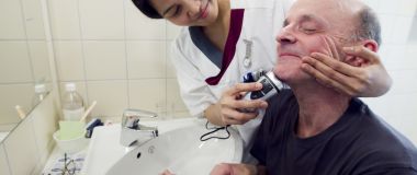 Helsefagarbeidar som hjelper ein mannleg pasient med barberingen.