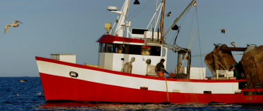 En rød fiskebåt til havs med en person ombord.