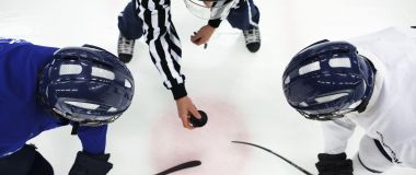 En ishockeydommer dropper pucken mellom to spillere.