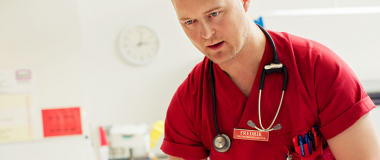 Sykepleier i rød uniform, stetoskop rundt halsen