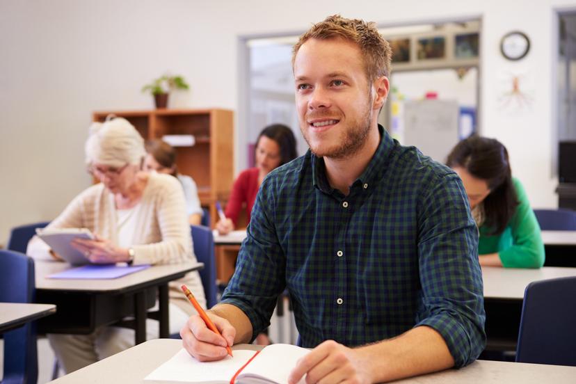 Mann med notatblokk og penn sitter i klasserom